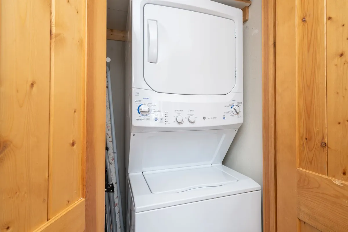 This image features a stacked washer and dryer tucked behind wooden doors, illustrating a dedicated laundry space within the home. The area is functional and neatly organized, ideal for families and longer stays.