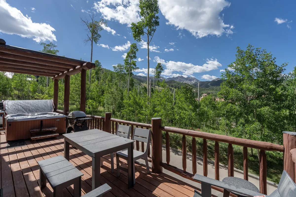 This image captures an outdoor seating area adjacent to a private hot tub, with sweeping mountain views in the background. The deck is elevated, offering a sense of privacy above neighboring homes, and the setting is bathed in natural light, emphasizing the tranquil and scenic atmosphere.