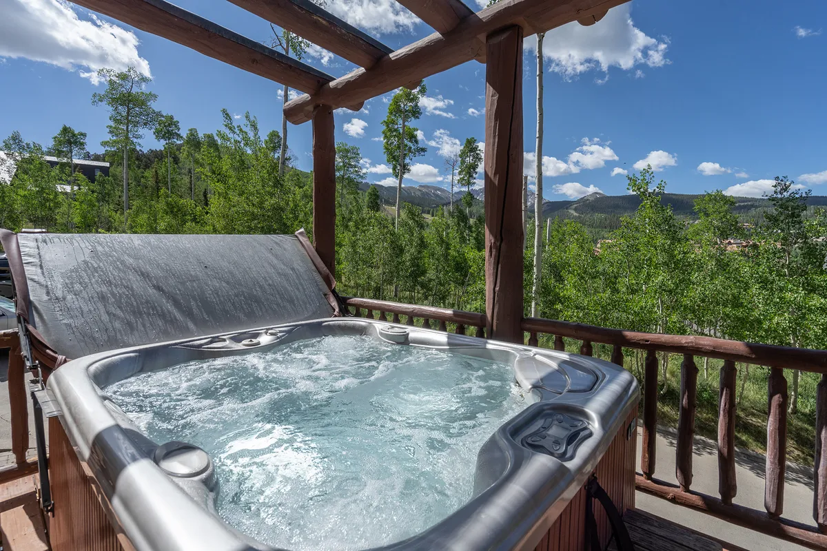 The photo showcases a hot tub set against a backdrop of mountains and surrounded by trees, inviting guests to relax and enjoy the view. The tranquil mood is perfect for morning coffee or evening soaks, and the image conveys privacy and serenity.