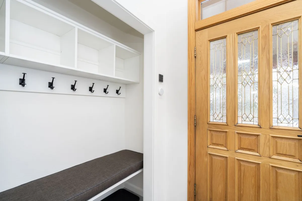 This image captures the entryway with a wooden door, bench seating, and hooks for coats and bags. The space is designed for guests to comfortably enter, store outerwear, and prepare for outings, conveying a sense of coming home after a day of adventure.