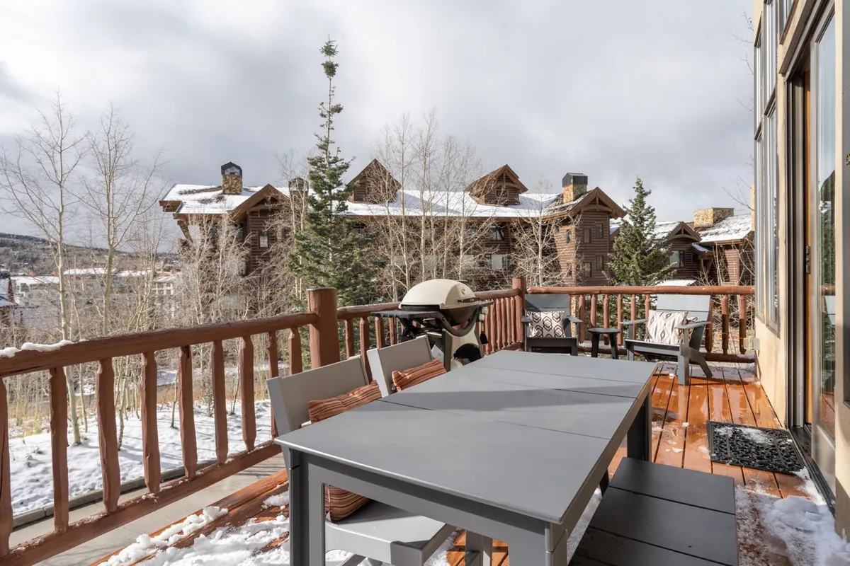 An inviting outdoor dining table and grill are set on a deck with panoramic mountain views and surrounded by trees, creating an ideal spot for sunset barbecues and group meals in nature.