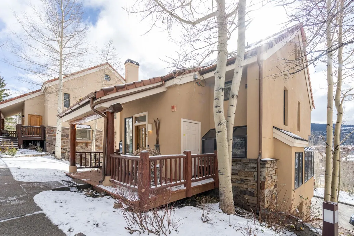 A cozy exterior shot of Ridgeline Retreat’s wooden deck, set against aspen trees and stone accents. The deck overlooks a serene mountain landscape, inviting guests to relax and enjoy the peaceful surroundings. Warm ambient light suggests sunset, enhancing the romantic ambiance.