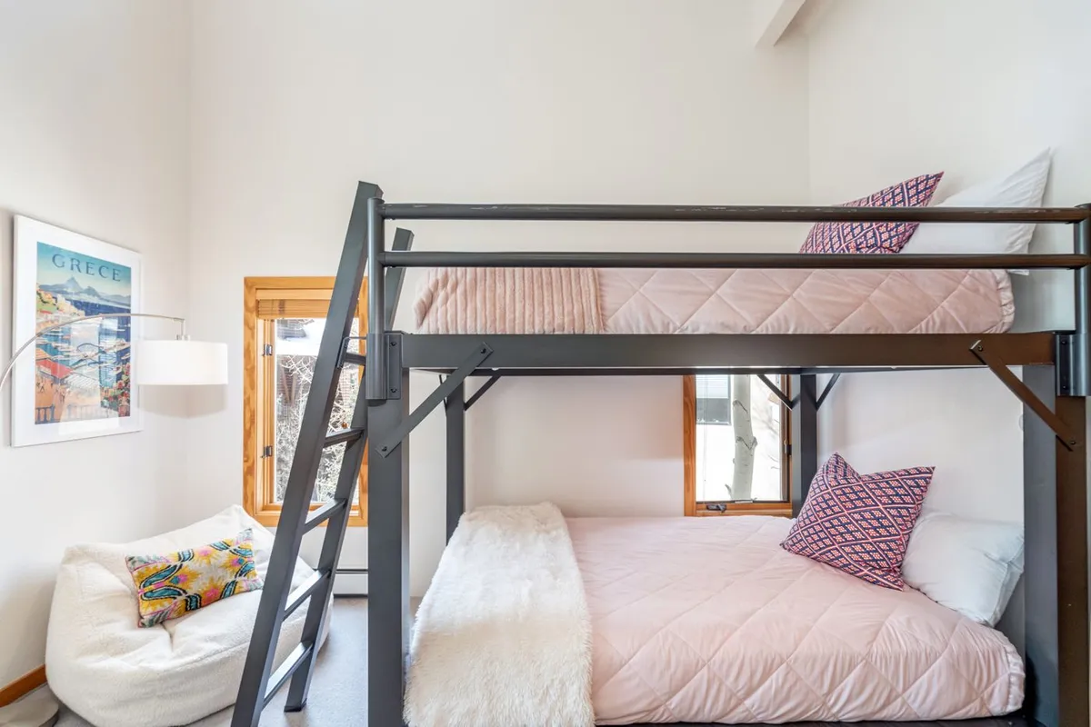 A playful bedroom with a queen-over-queen bunk bed, bean bag chair, large windows, and cheerful artwork. The space is designed for both sleep and relaxation, offering flexibility for groups or families.